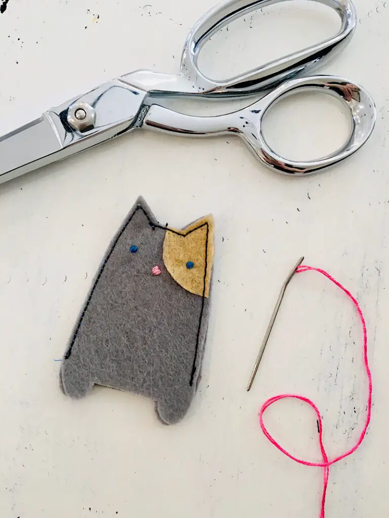 felt cat finger puppet with eye patch scissors and needle on white table