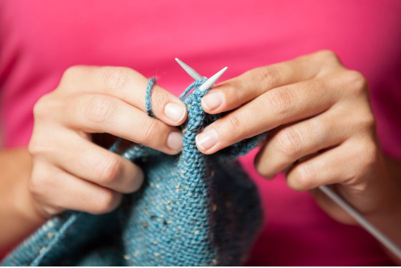 womans hands holding knitting needles with blue yarn