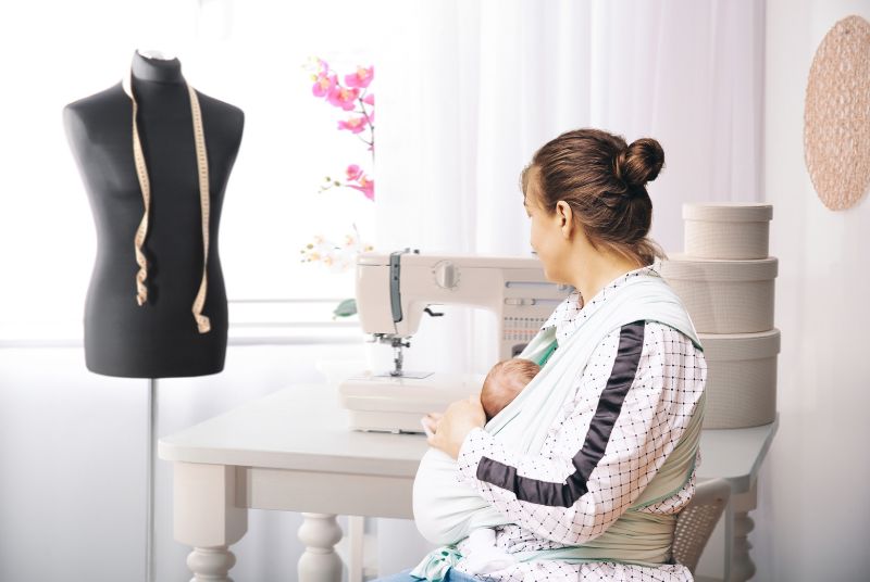 woman babywearing while sitting at desk with sewing machine
