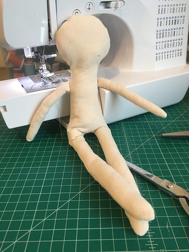 completed blank doll body sitting against sewing machine