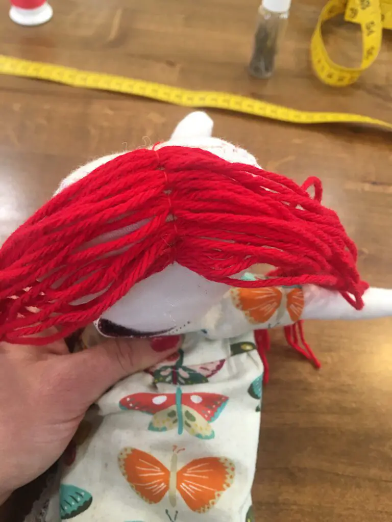sewing red yarn on a doll's head