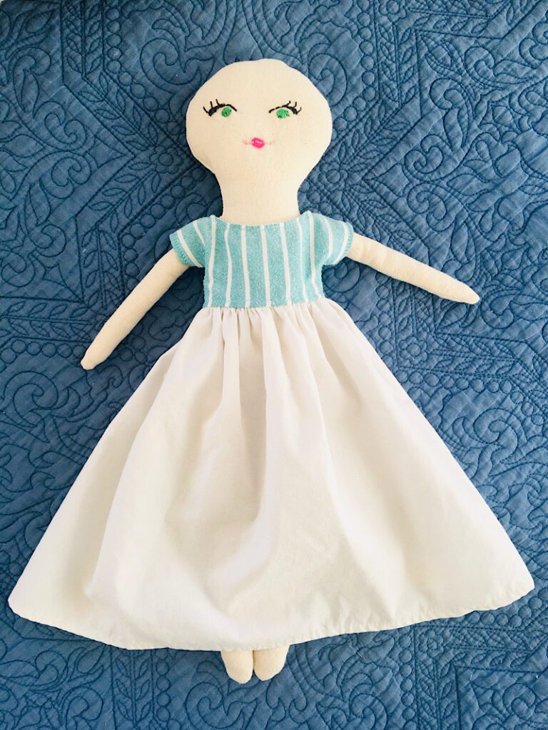 finished rag doll dress on cloth doll laying on bed