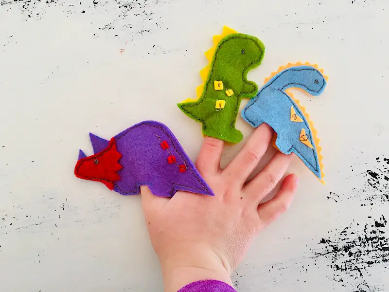 childs hand holding felt dinosaur finger puppets