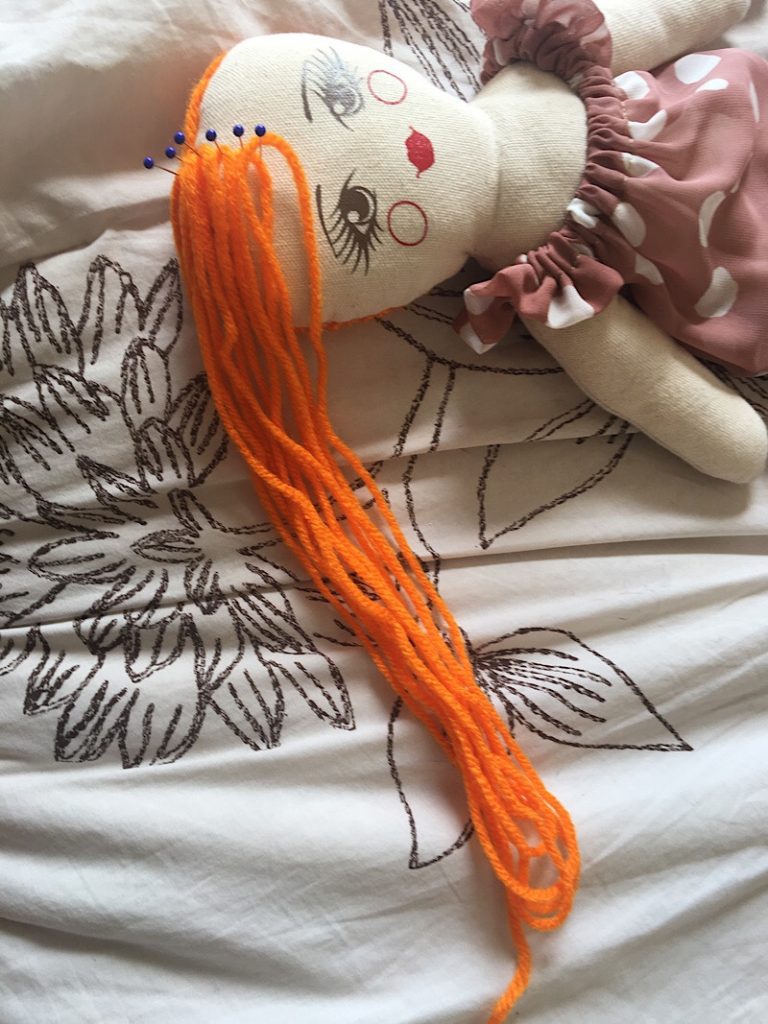 Pin & Sew yarn doll hair method, cloth doll on bed with orange hair