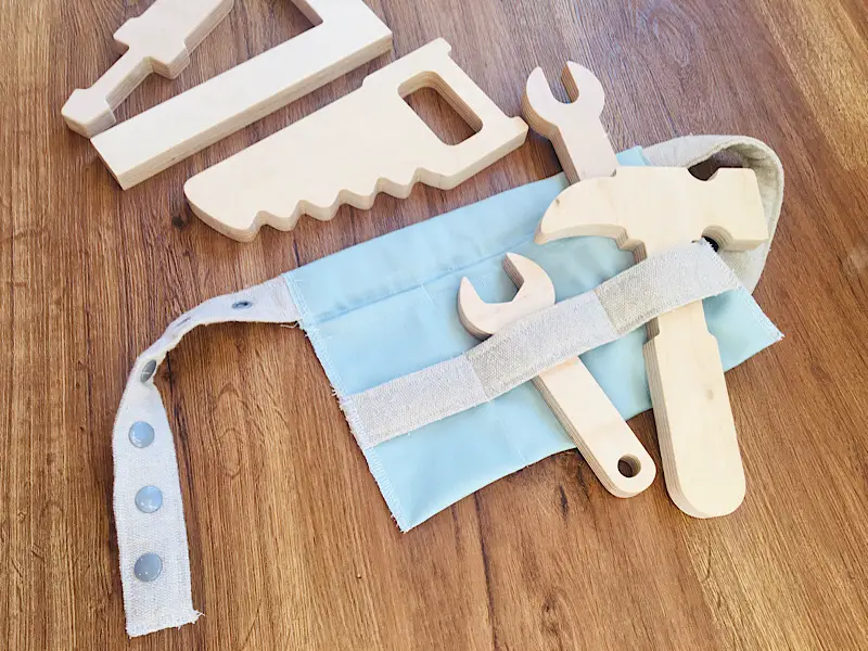 DIY toddler tool belt made from blue and cream canvas fabric, on floor with wooden toy tools
