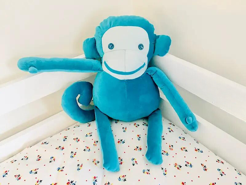 blue fabric stuffed monkey sitting on a bed
